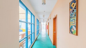A long hallway with large windows, a green carpet, and a colorful wall art piece. - HI Faro- Pousada de Juventude - Hostel (Faro)