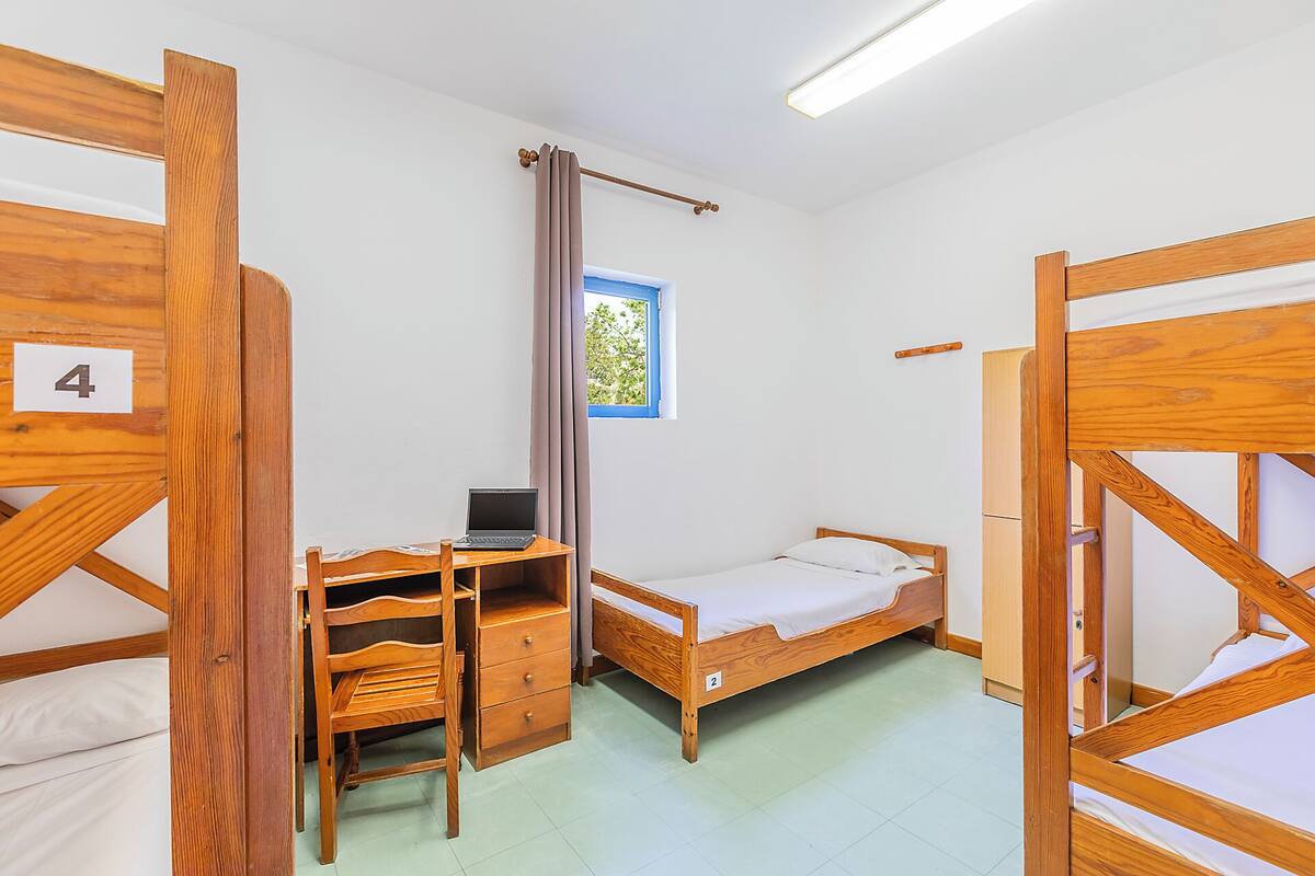 Une chambre de dortoir avec des lits superposés, un bureau avec un ordinateur portable, une fenêtre avec des rideaux et une porte portant le numéro 4.