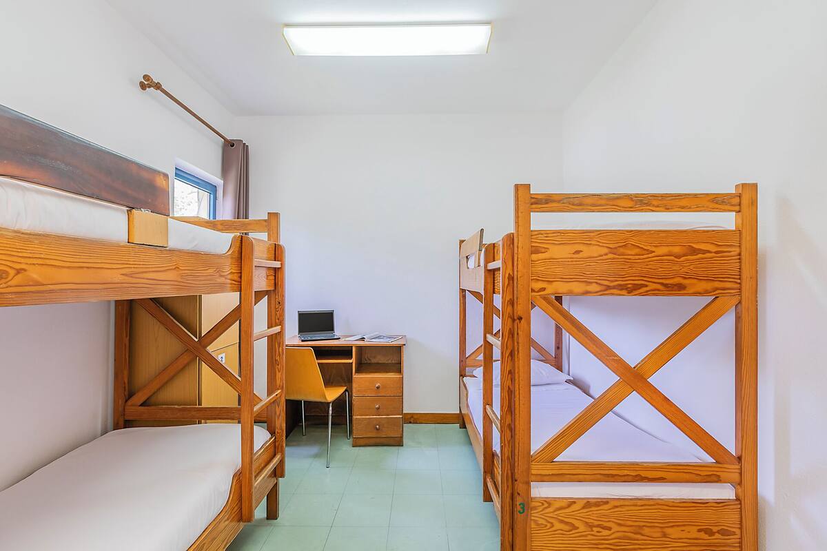 Une chambre de dortoir avec des lits superposés, un bureau, une chaise et un ordinateur portable.