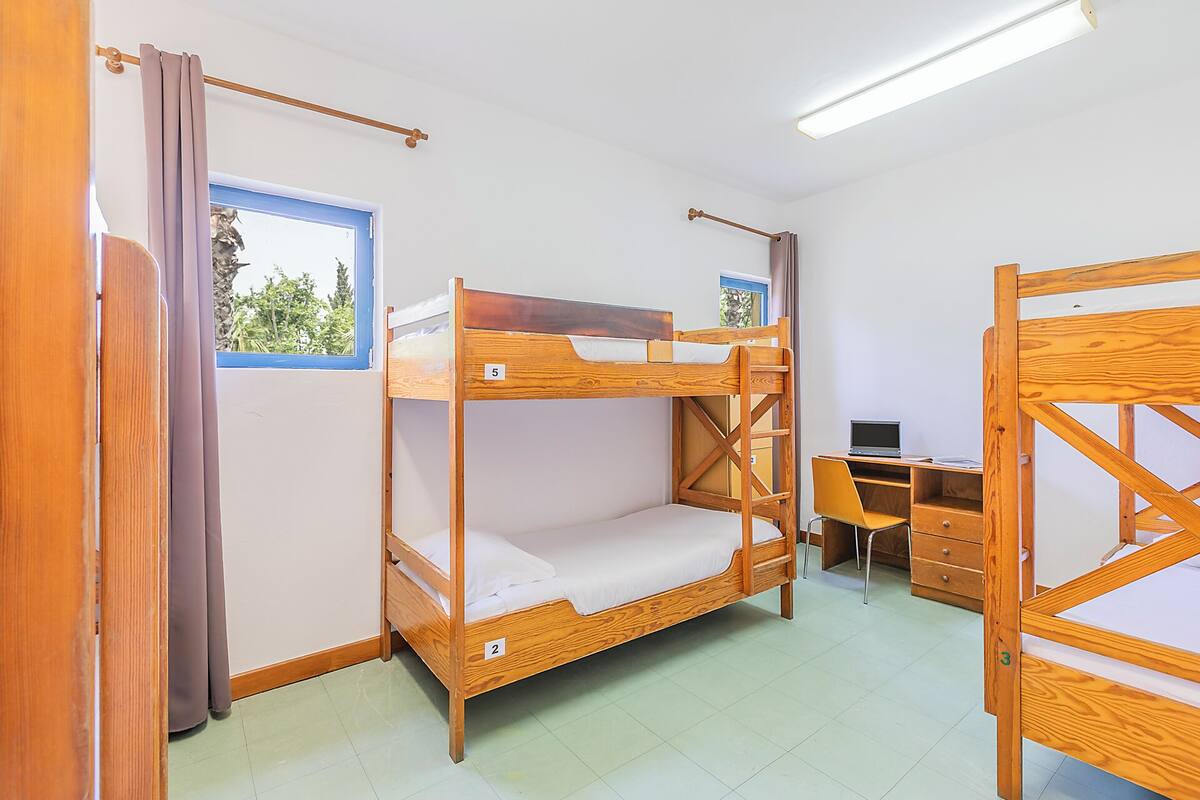 Une chambre avec un lit superposé, un bureau et une chaise, une fenêtre avec vue et un rideau.