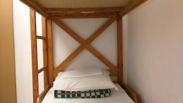 A small, wooden-framed room with a single bed, white bedding, and a checkered blanket.