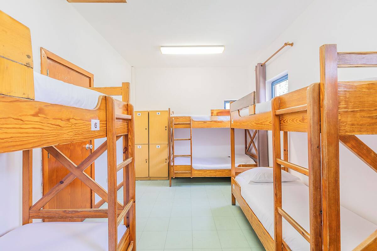 Une chambre de dortoir avec des lits superposés, des casiers en bois et une porte portant un numéro.
