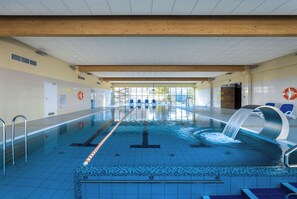 Ein Schwimmbecken mit deutlichen Bahnen, einem Wasserspiel und blauen Stühlen entlang der Seiten.