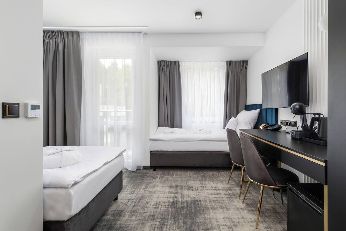 A hotel room with a bed, a desk, a chair, a TV, and a window with curtains.