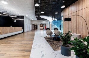 A modern lobby with a reception desk, seating area, and a staircase leading to upper floors.