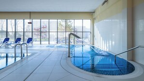 Une piscine intérieure avec des parois en verre transparent, de l’eau bleue et quelques chaises longues.