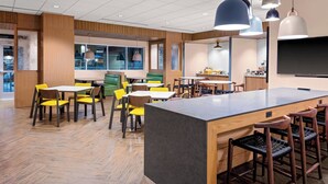 A modern hotel lobby with wooden flooring, yellow and brown chairs, a central island with bar stools, and pendant lighting. - Fairfield Inn & Suites by Marriott Memphis Collierville (Collierville)
