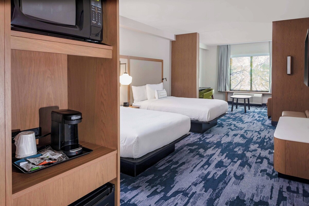 A hotel room with two beds, a coffee maker, a desk, and a window with a view.