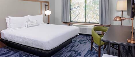 A hotel room with a bed, a desk, a chair, a window with curtains, and a lamp.