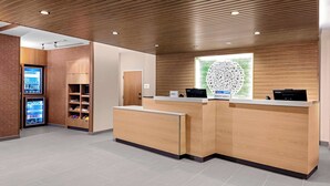 A reception area with wooden panel walls, a reception desk, a digital screen, and a vending machine. - Fairfield Inn & Suites by Marriott Memphis Collierville (Collierville)