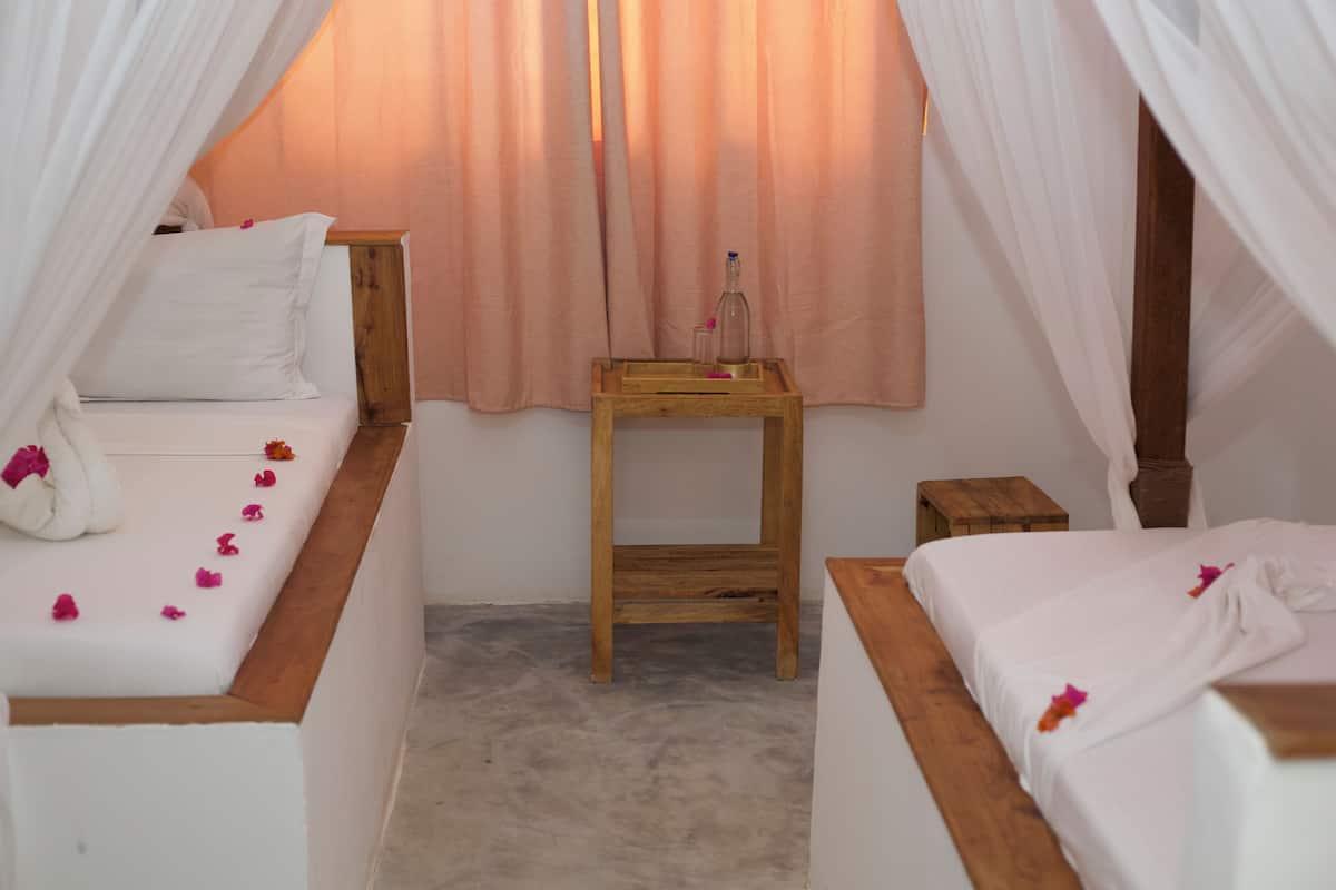 Una habitación acogedora con dos camas, una mesita de noche de madera y una pequeña mesa con una botella y un vaso.