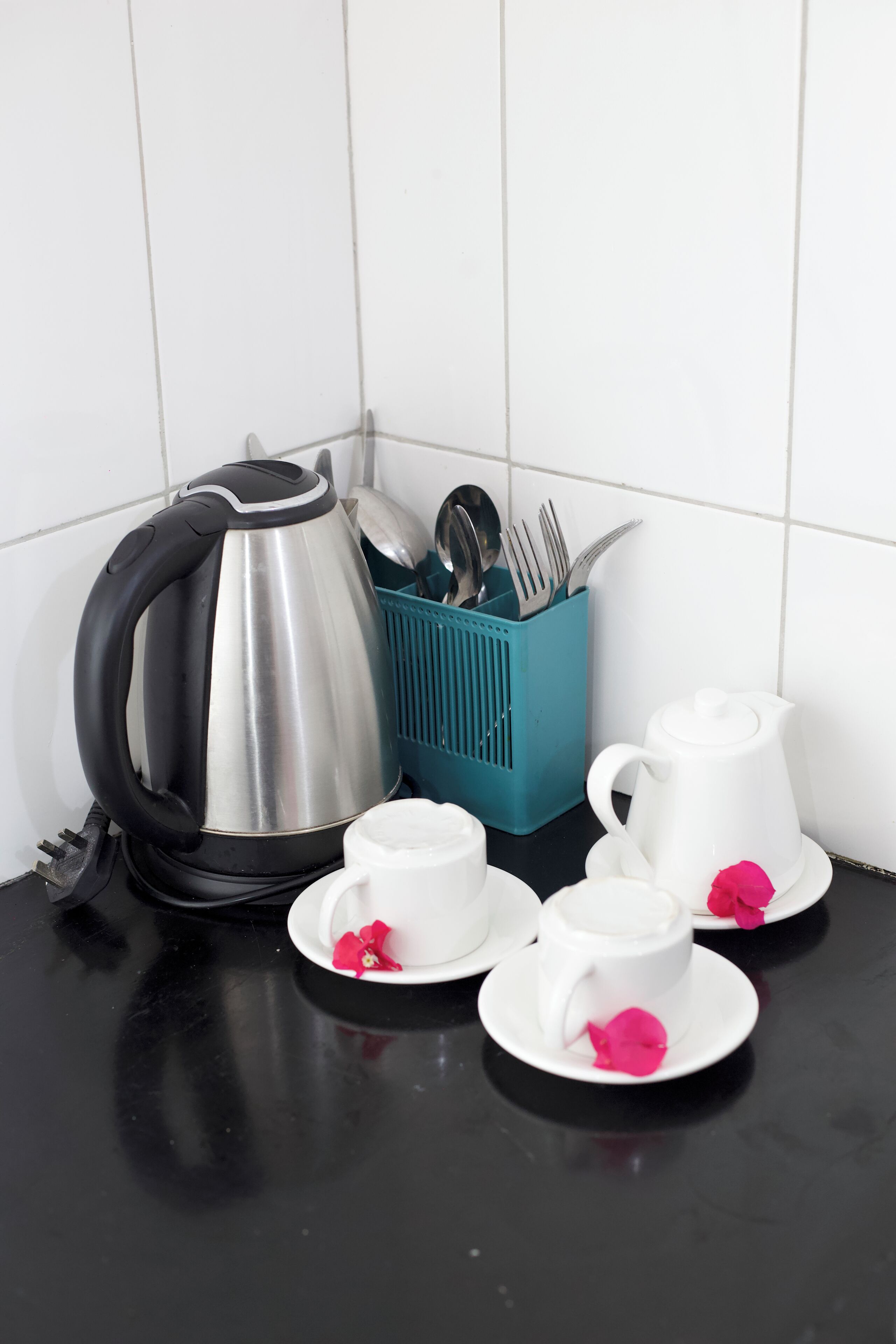 Un plan de travail de cuisine avec une bouilloire, une théière, des tasses et un porte-ustensiles.