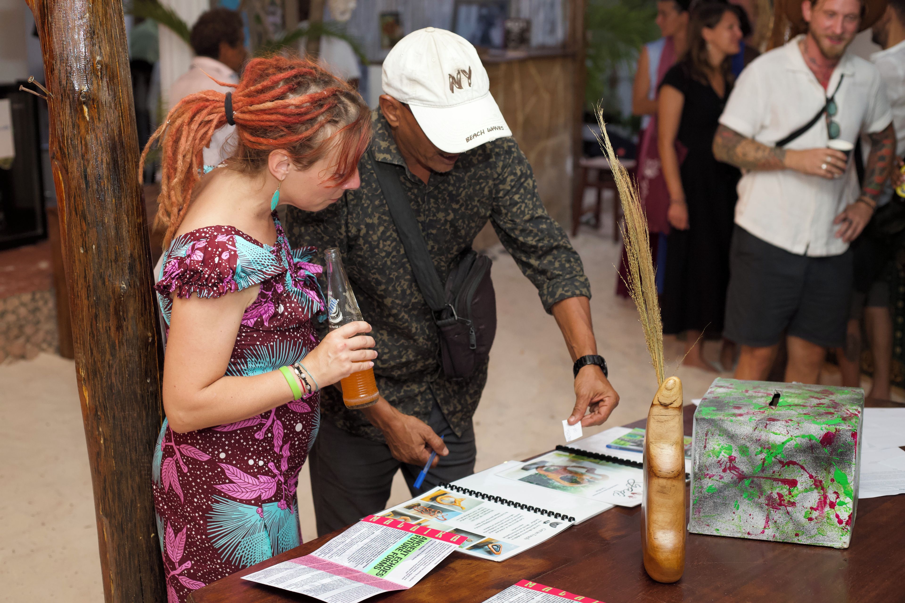 A person holding a bottle at a booth with a table displaying brochures and a wooden object.