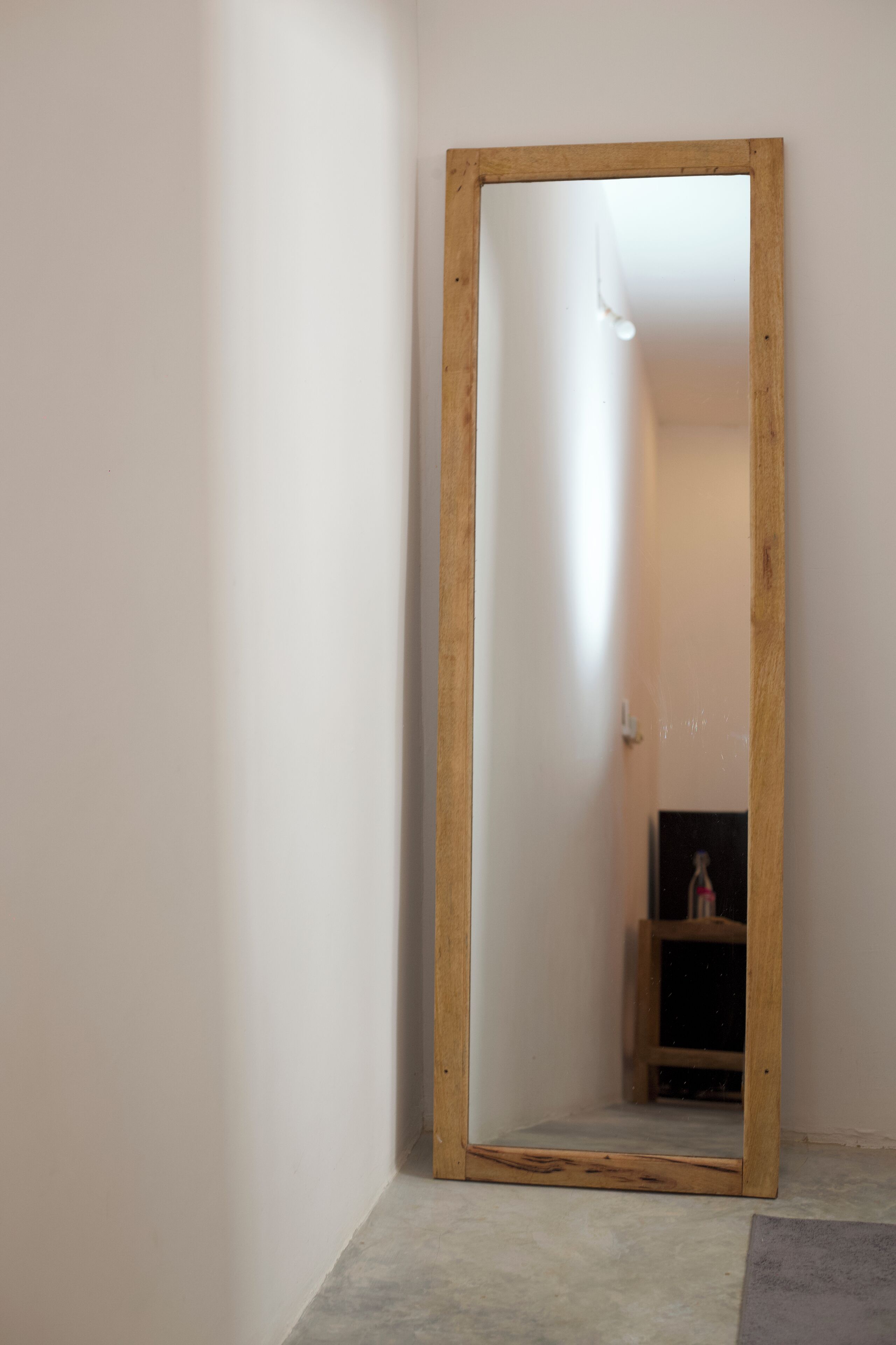 A mirror with a wooden frame in a room with plain walls and a concrete floor.