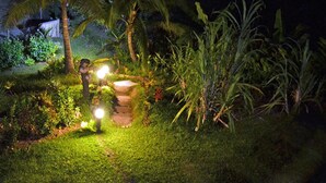A nighttime garden with a stone pathway, palm trees, and illuminated lights. - Fijian Oasis (Korolevu)