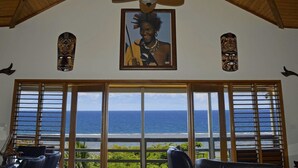 A room with a large window overlooking the ocean, wooden furniture, and two decorative masks on the wall. - Fijian Oasis (Korolevu)