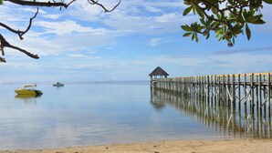 A beach with a wooden pier extending into calm waters, a small boat, and a thatched-roof structure. - Fijian Oasis (Korolevu)