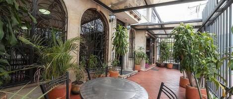 Un espace patio intérieur doté d’un plafond en verre, de plantes en pot et de tables en métal.