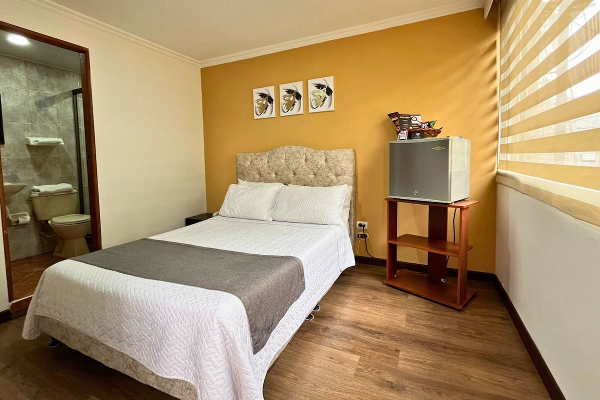 Een slaapkamer met een bed, een televisie op een dressoir en een badkamer zichtbaar door een open deur.