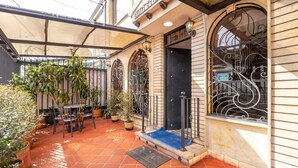 A courtyard with terracotta tiles, potted plants, a covered seating area, and a black door with a blue mat. - Tita´s House Bogotá (Bogotá)