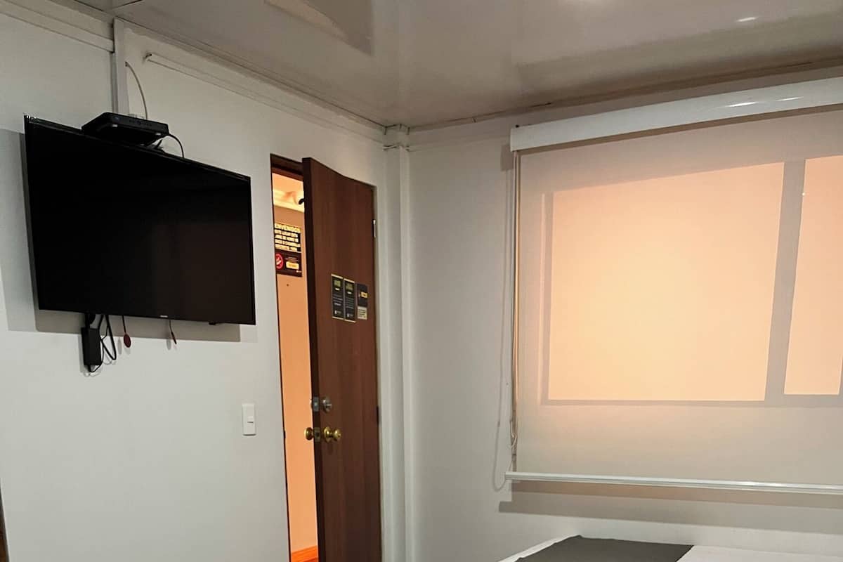 Een hotelkamer met twee bedden, een aan de muur bevestigde televisie en een raam met zonwering.