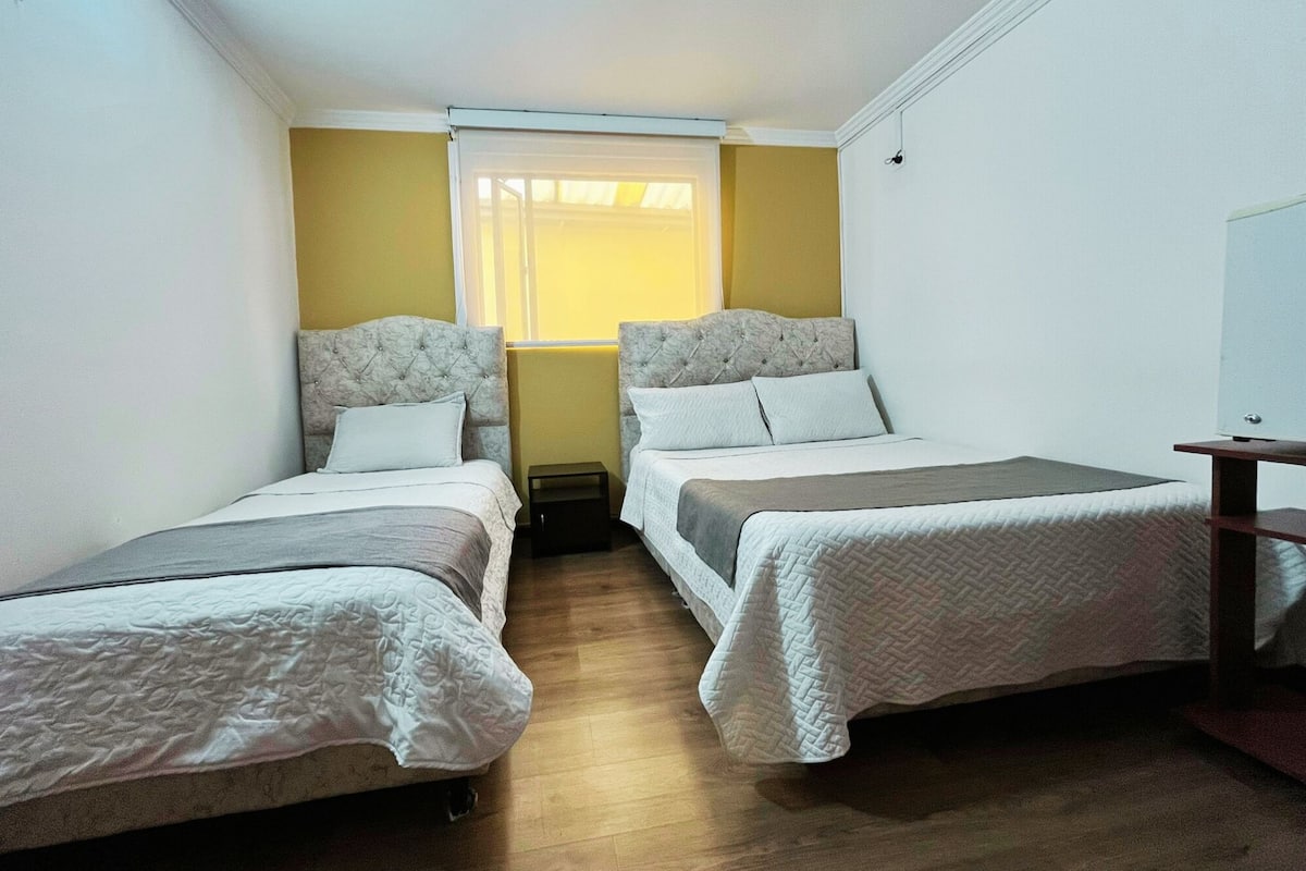 Een kleine, compacte kamer met twee eenpersoonsbedden, een raam met zonwering en een tafeltje.