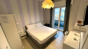 A hotel room with a bed, a desk, a mirror, and a window with a view of buildings. - F Rooms (Naples)