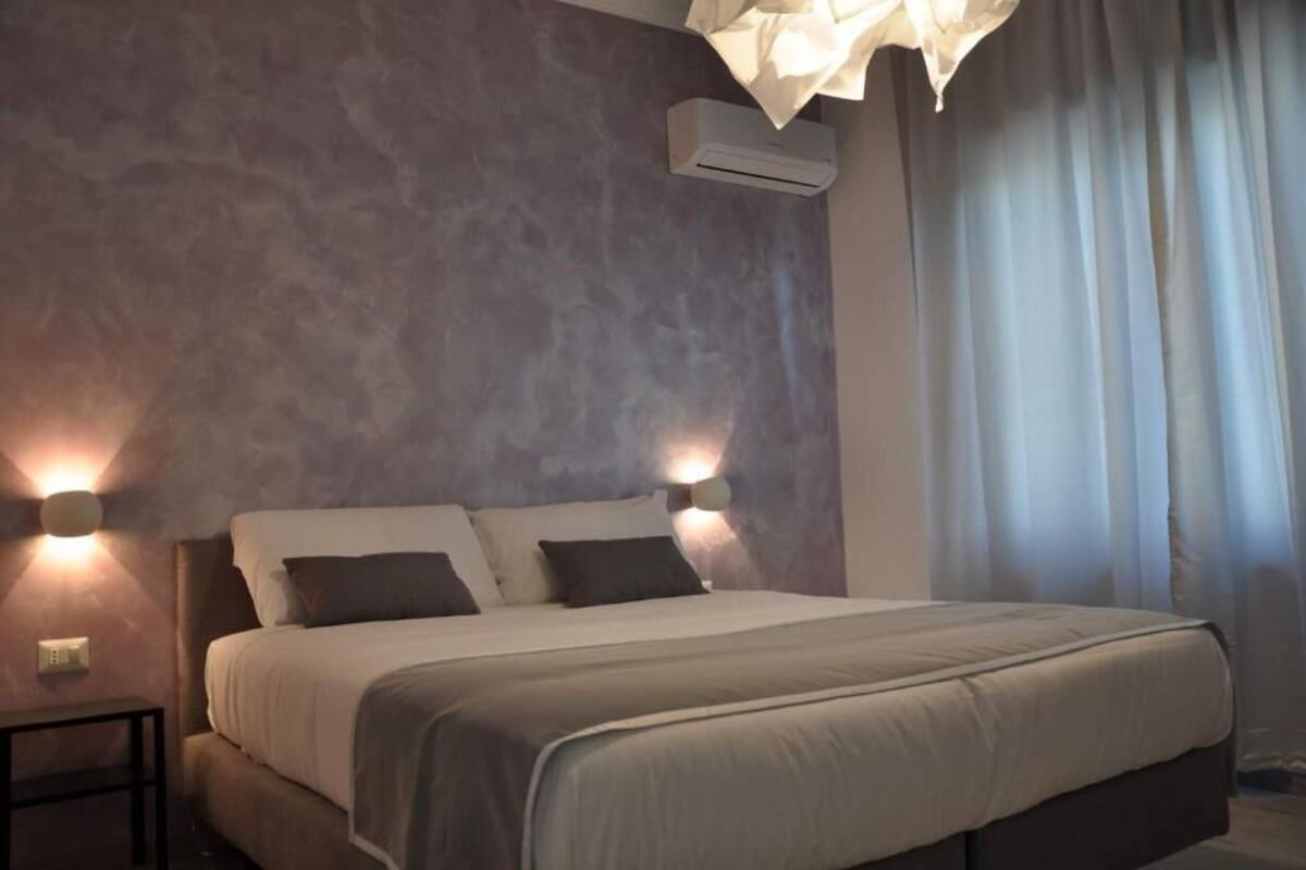 A bedroom with a large bed, two wall-mounted lights, an air conditioning unit, and a window with curtains.
