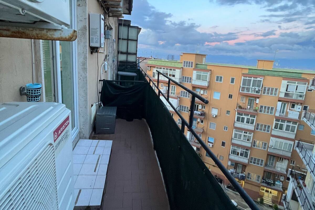 A balcony with a view of adjacent buildings, a metal railing, and a utility meter.