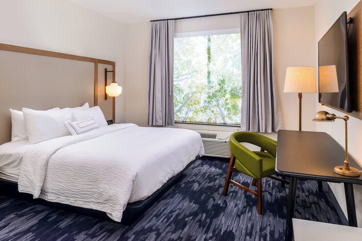 Habitación de hotel con cama, escritorio, silla, televisor y ventana con cortinas.