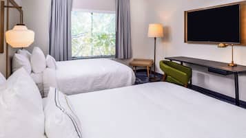Habitación de hotel con dos camas, un escritorio, una silla, un televisor y una ventana con cortinas.