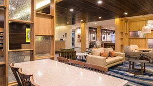 Un moderno vestíbulo de hotel con zona de comedor central, sofás y bar.