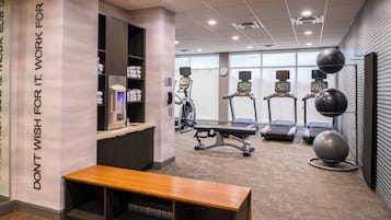 Academia com esteiras, bolas de exercício e um banco.
