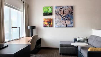 Une chambre d’hôtel moderne, équipée d’un bureau, d’un canapé gris, d’une petite table ronde et de trois tableaux accrochés au mur.
