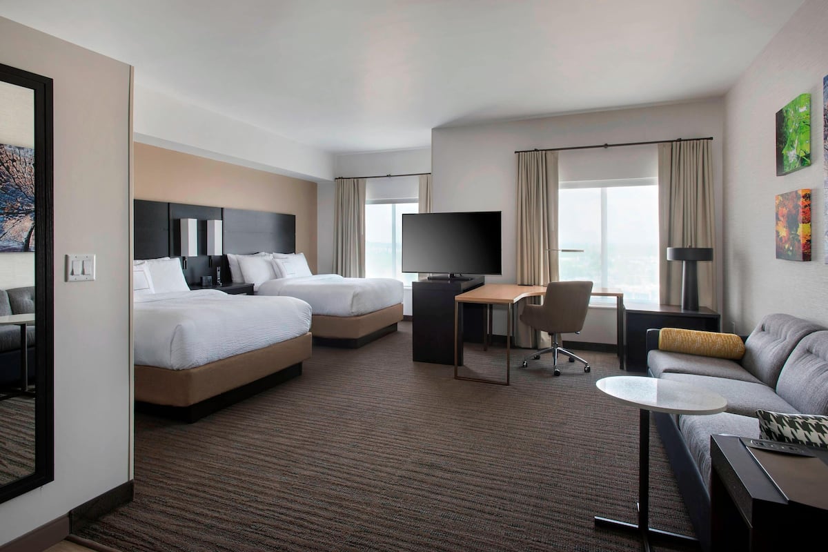 A hotel room with two beds, a desk, a TV, and a sofa.