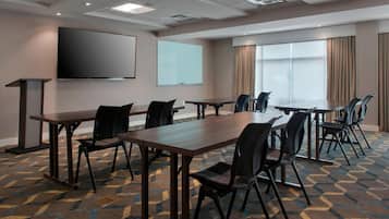 Un salón de conferencias con una gran mesa, sillas, una pantalla de proyector, una pizarra y suelo alfombrado.