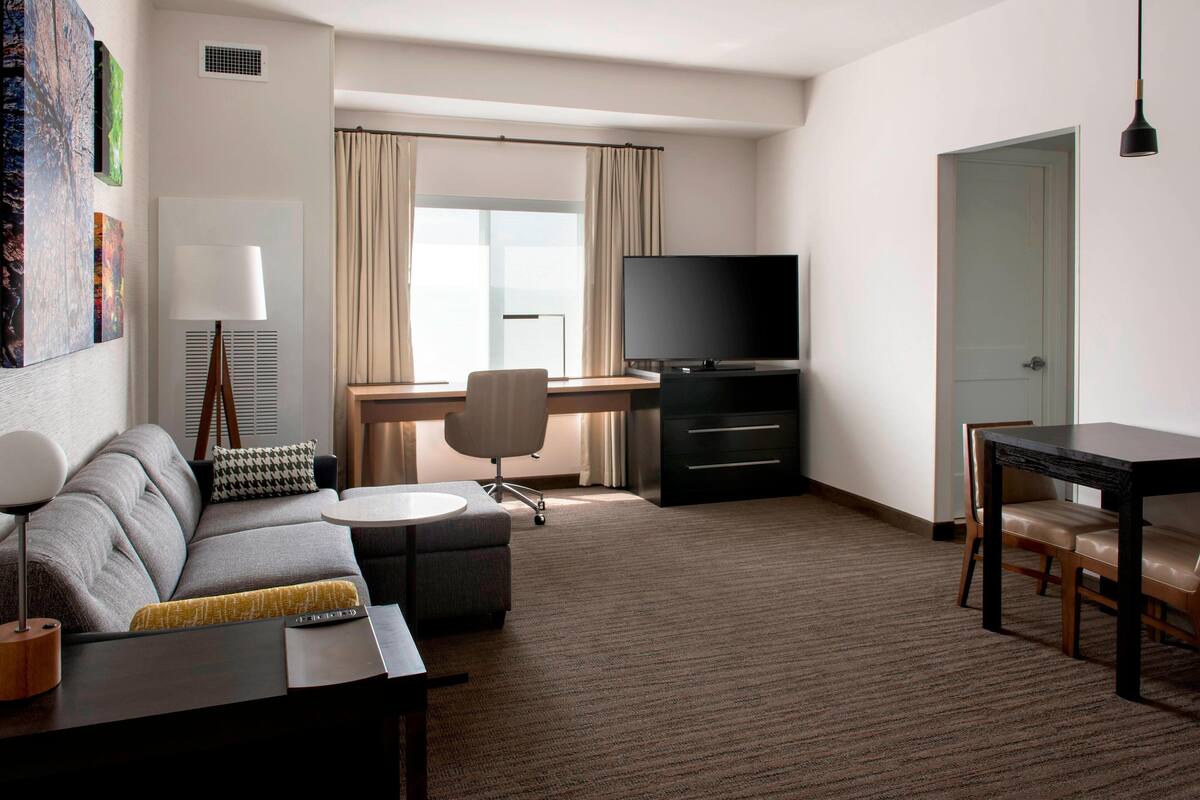 A modern hotel room with a sofa, a desk, a television, and a dining table.