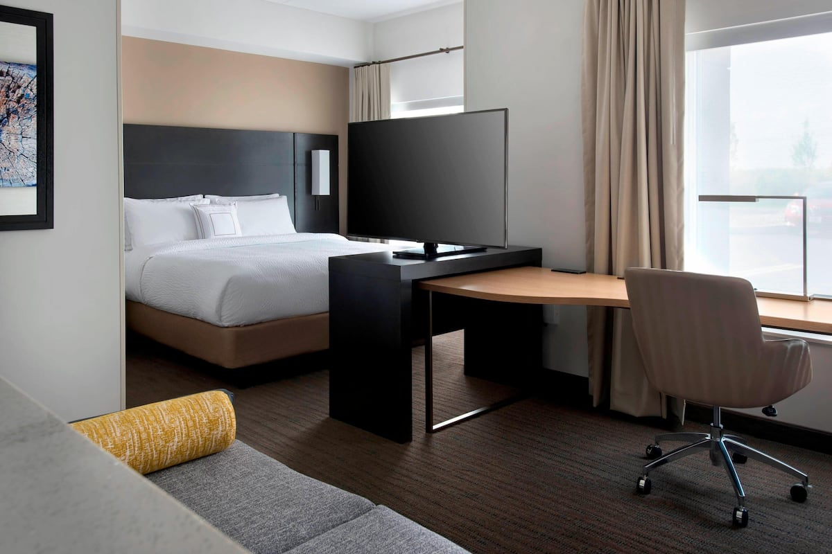 A modern hotel room with a bed, a desk, a chair, and a television.