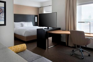A modern hotel room with a bed, a desk, a chair, and a television.