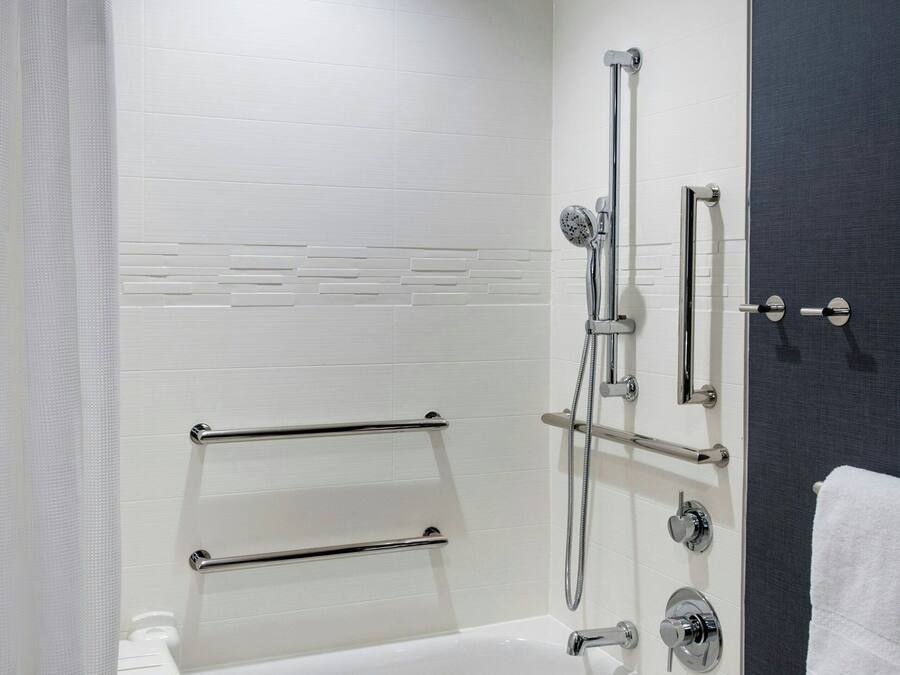 A modern bathroom with a white bathtub, a shower with a handheld showerhead, and a towel rack.
