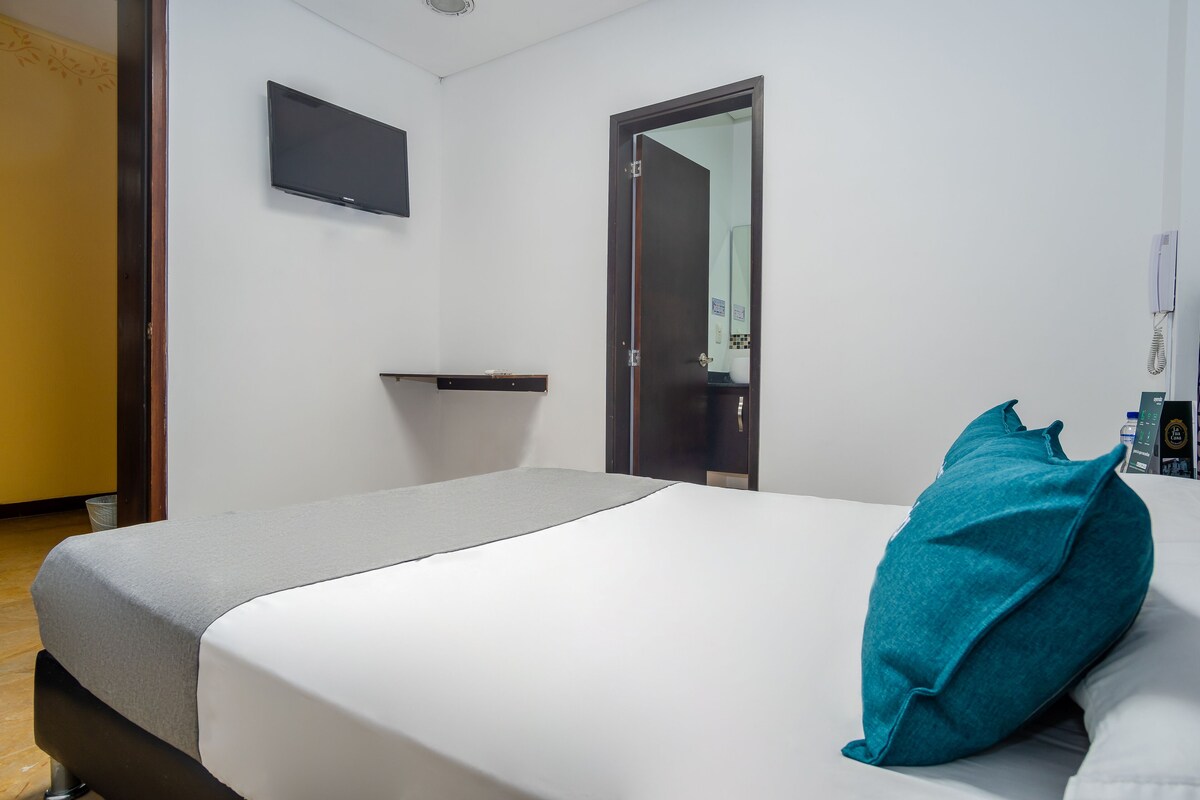 Habitación de hotel con cama, televisor de pantalla plana montado en la pared, una puerta y una mesita de noche.