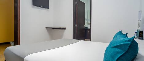 Ein Hotelzimmer mit Bett, Flachbildfernseher an der Wand, einer Tür und einem Nachttisch.