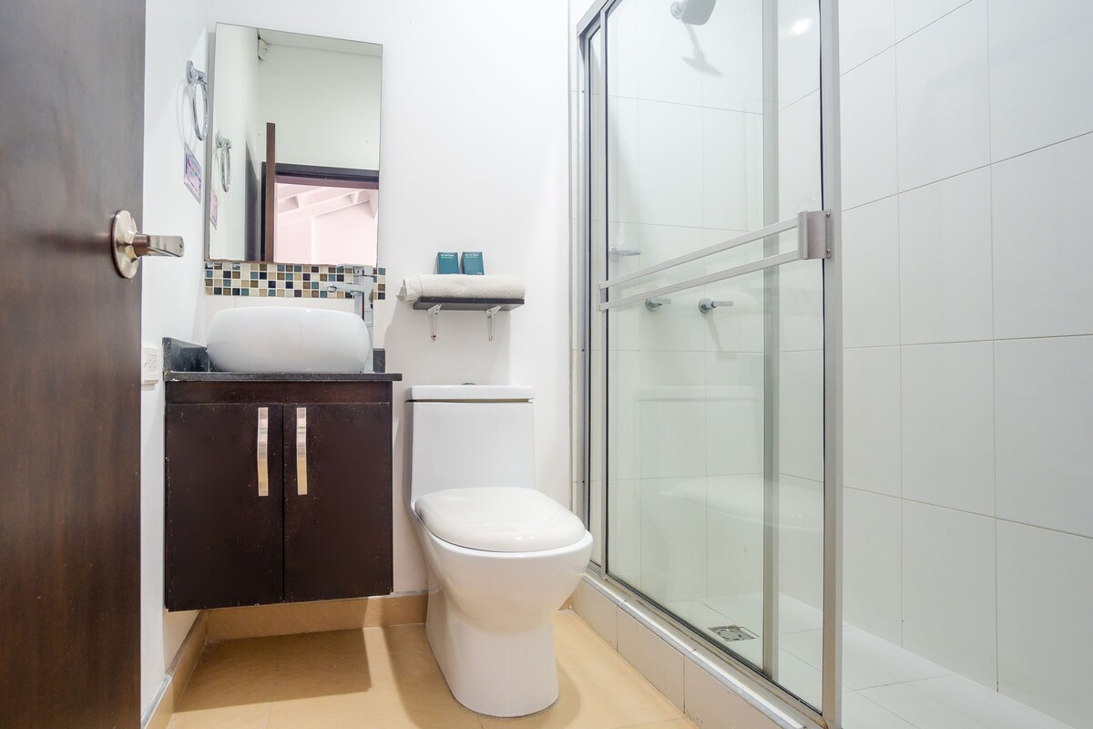 Un baño con inodoro, lavamanos, espejo y zona de ducha.
