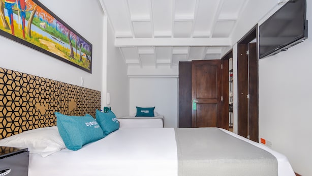 A hotel room with a bed, a headboard with a geometric pattern, a painting on the wall, and a television. - Ayenda La Tua Casa (Bogotá)