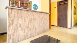 A reception area with a wooden reception desk, a wall-mounted artwork, and a sign for 'ayenda hotels'. - Ayenda La Tua Casa (Bogotá)