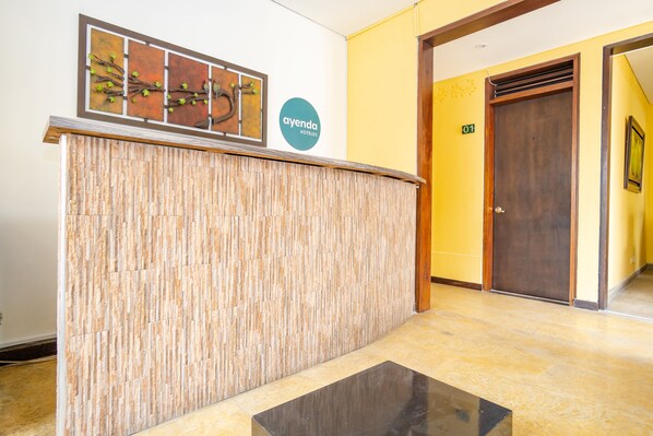 A reception area with a wooden reception desk, a wall-mounted artwork, and a sign for 'ayenda hotels'. - La Tua Casa (Bogotá)