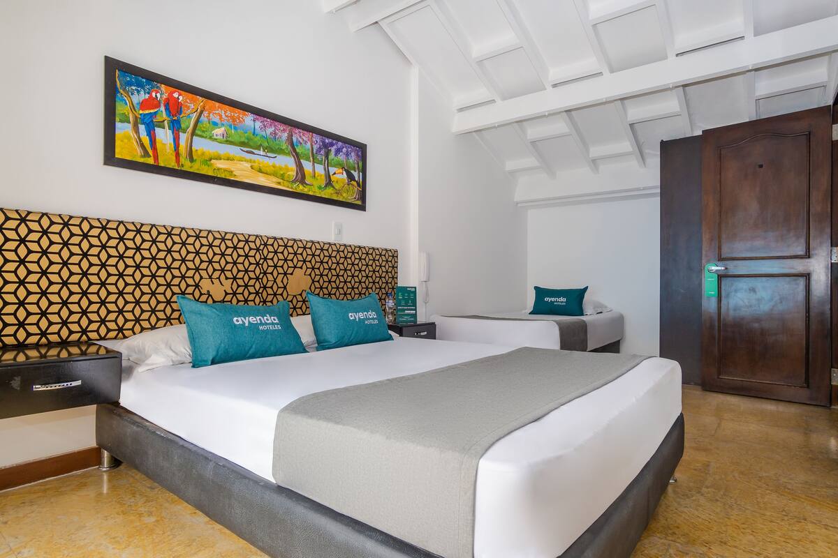 A hotel room with a large bed, a headboard with a geometric pattern, a painting above the bed, and a wooden door.