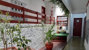 A corridor with a tiled floor, a wooden bench, potted plants, a stone wall, and a red door. - Hostal Blanco Apart-Hotel (Florianópolis)