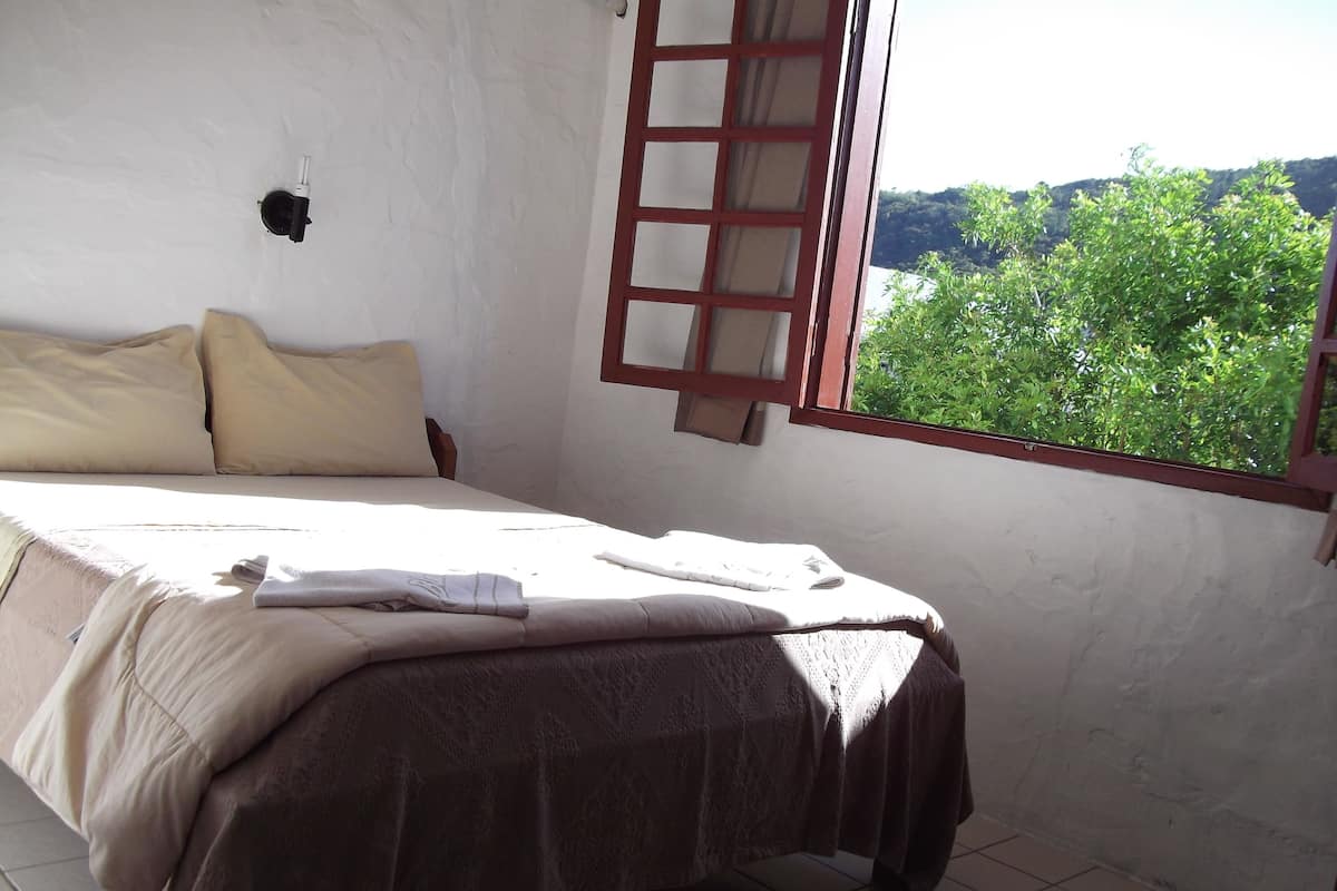 Une chambre à coucher avec un lit, une fenêtre donnant sur un paysage verdoyant et un luminaire fixé au mur.