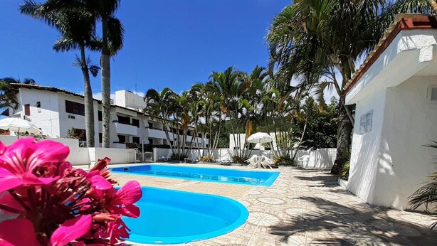 A swimming pool with a tiled deck, surrounded by palm trees and white buildings. - Hostal Blanco Apart-Hotel (Florianópolis)